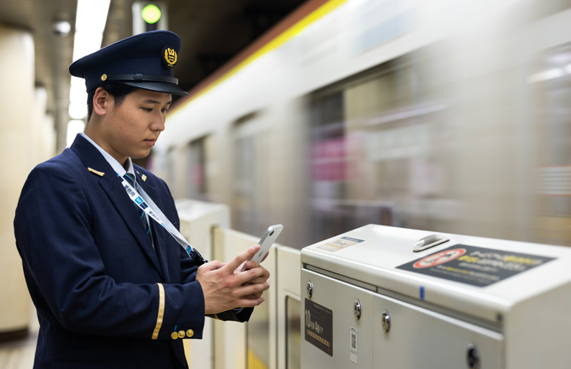 Um atendente da estação está na plataforma usando o iPhone para escanear um código QR enquanto um trem passa.