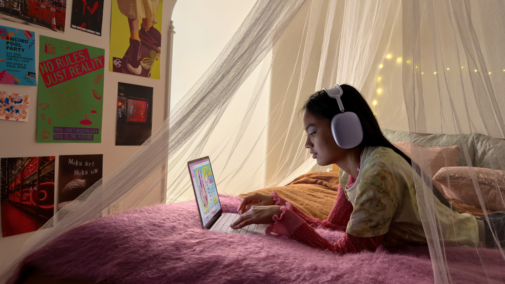 Une jeune personne dans sa chambre, portant un casque d’écoute, utilise un MacBook Neo rose poudré pour prendre rendez-vous pour une manucure
